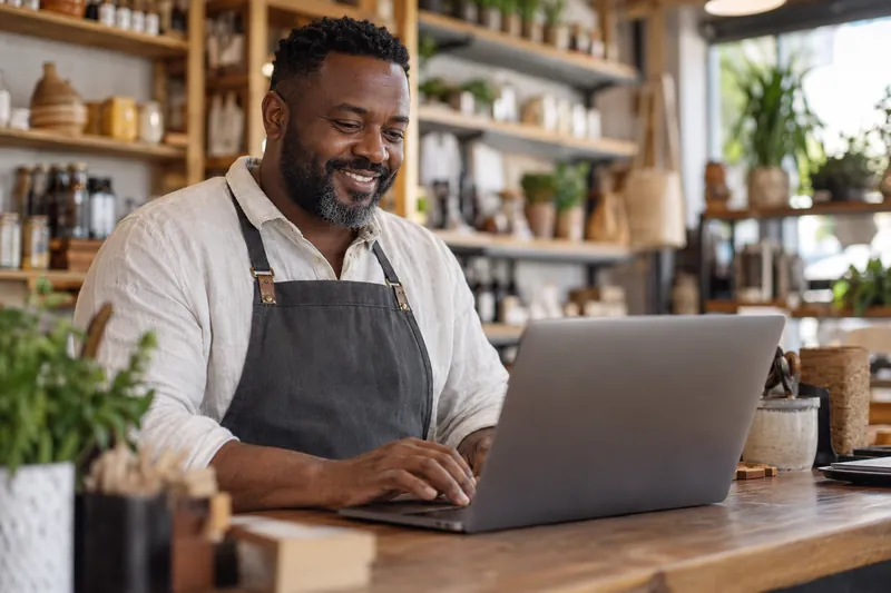 Small business owner reviewing his books on a laptop at his shop counter